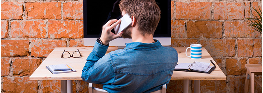Man on cell phone at desk in front of brick wall